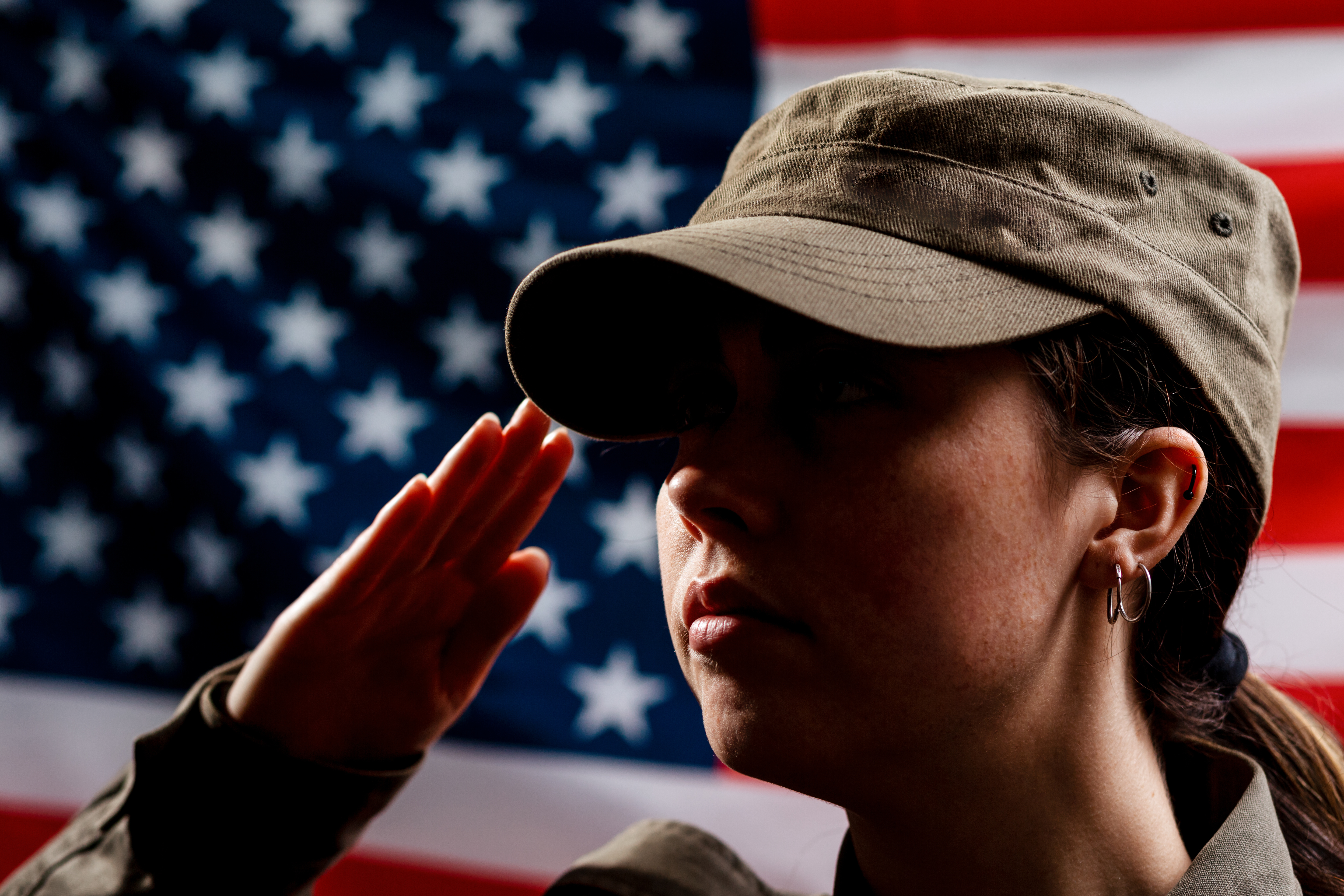  A portrait of female soldier in uniform salutes against the background of the American flag. 